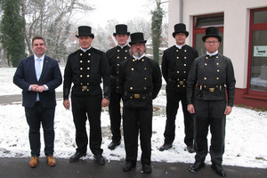 Sechs Männer, darunter fünf Schornsteinfeger stehen in einer Gruppe und schauen in die Kamera.