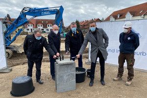 Vier Männer mit einem Hammer in der Hand stehen verteilt um den Grundstein herum.