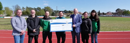 7 Personen stehen auf der Laufbahn im Premnitzer Stadion und die 3 in der Mitte halten den symbolischen Spendenscheck. - Klick öffnet Bildbetrachter