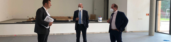 Drei Männer stehen im Halbkreis und unterhalten sich in der noch leeren neuen Halle.