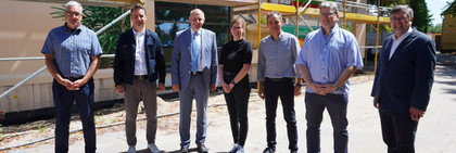 Eine Gruppe von sieben Menschen steht vor einem Baugerüst, das vor der Schule steht. An der Fassade ist ein Wandbild zu erkennen.