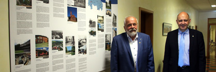 Zwei Männer stehen in einem Flur, an der Wand hängt eine Schautafel.