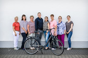 Acht Personen stehen vor einer Wand, davor steht ein Fahrrad - Klick öffnet Bildbetrachter