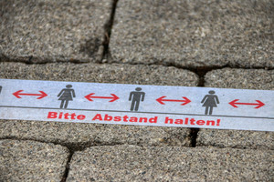 Eine Klebestreifen auf dem Boden mit der Aufschrift: Bitte Abstand halten!