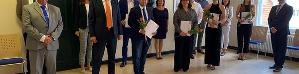 Die Absolventen sowie ihre Begleiter stehen mit Landrat Roger Lewandowski in einem Raum und schauen in die Kamera.