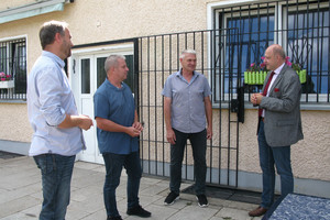 Landrat Lewandowski unterhält sich mit drei Mitgliedern des ESV Lok Elstal vor einem Vereinsgebäude.